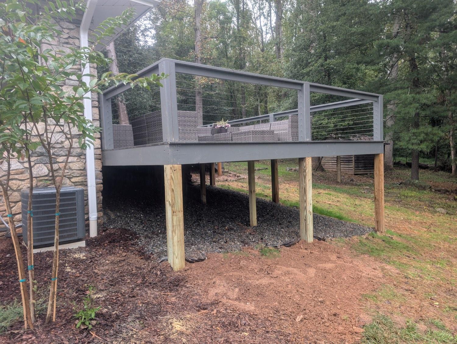 A raised grey deck with stainless cable railing, standing on new posts over a gravel bed.